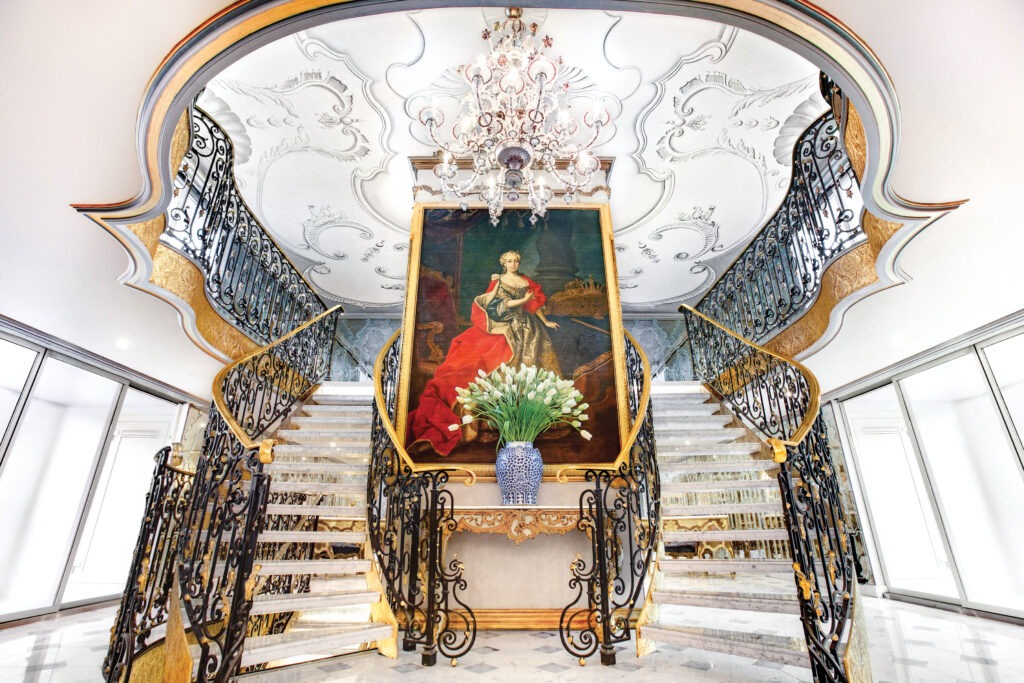 The ornate lobby and grand double staircase of S.S. Maria Theresa, with a framed portrait of Auntie Marie herself, looking quite imperial between the cut flowers and crystal chandelier. CREDIT: Uniworld. 