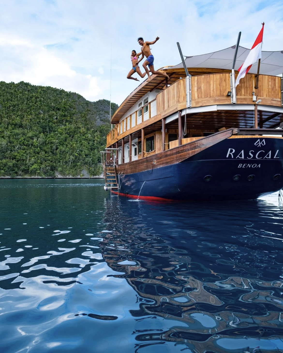 Delighted travelers leap into the water of a tropical bay off a Rascal Voyages ship