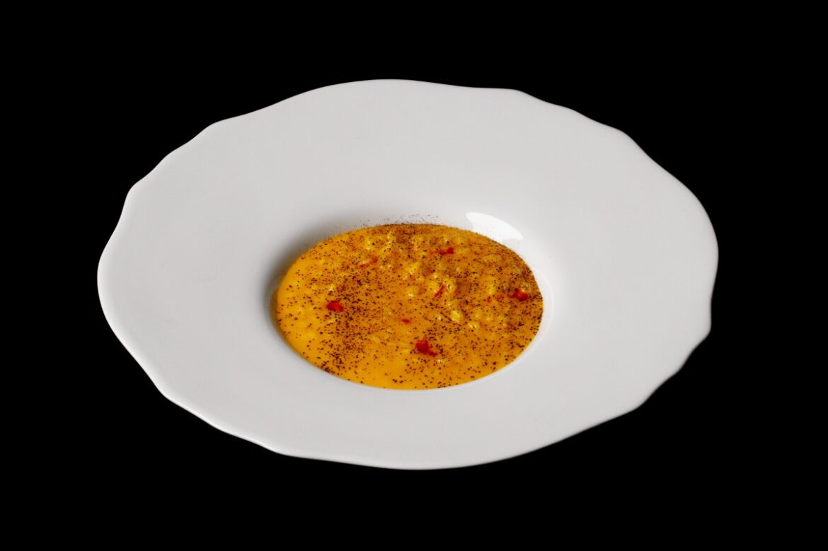 Saffron risotto with licorice powder, served at Osteria d’Ovidio aboard Crystal Cruises: yellow rice on a wide, white plate against a stark, black background.